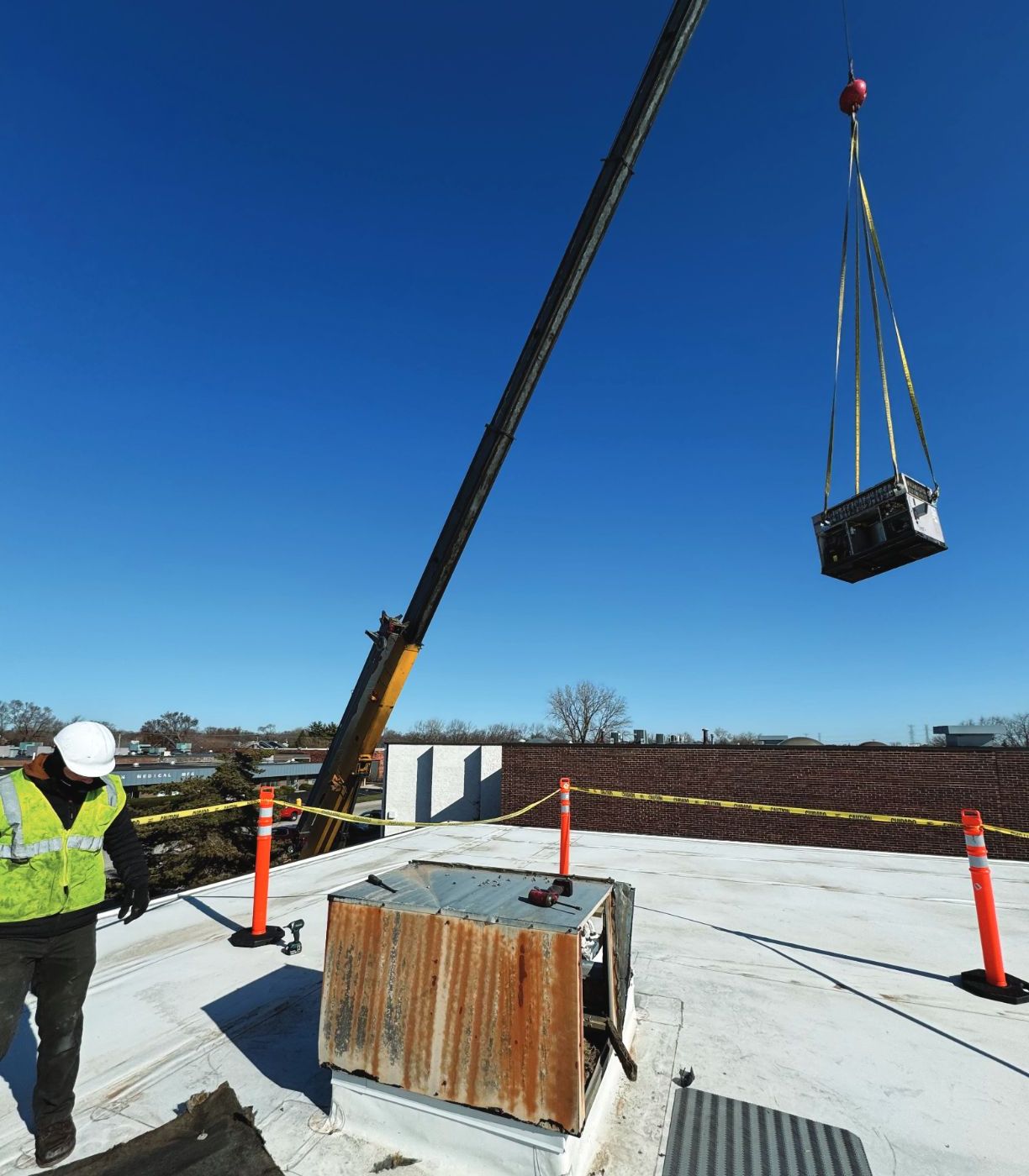 Crane boom lifting a rooftop unit over a medical building